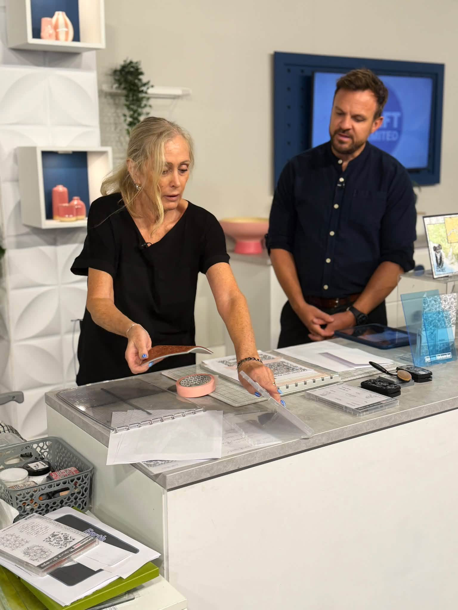 Karen demonstrating at the studio craft table with the presenter watching