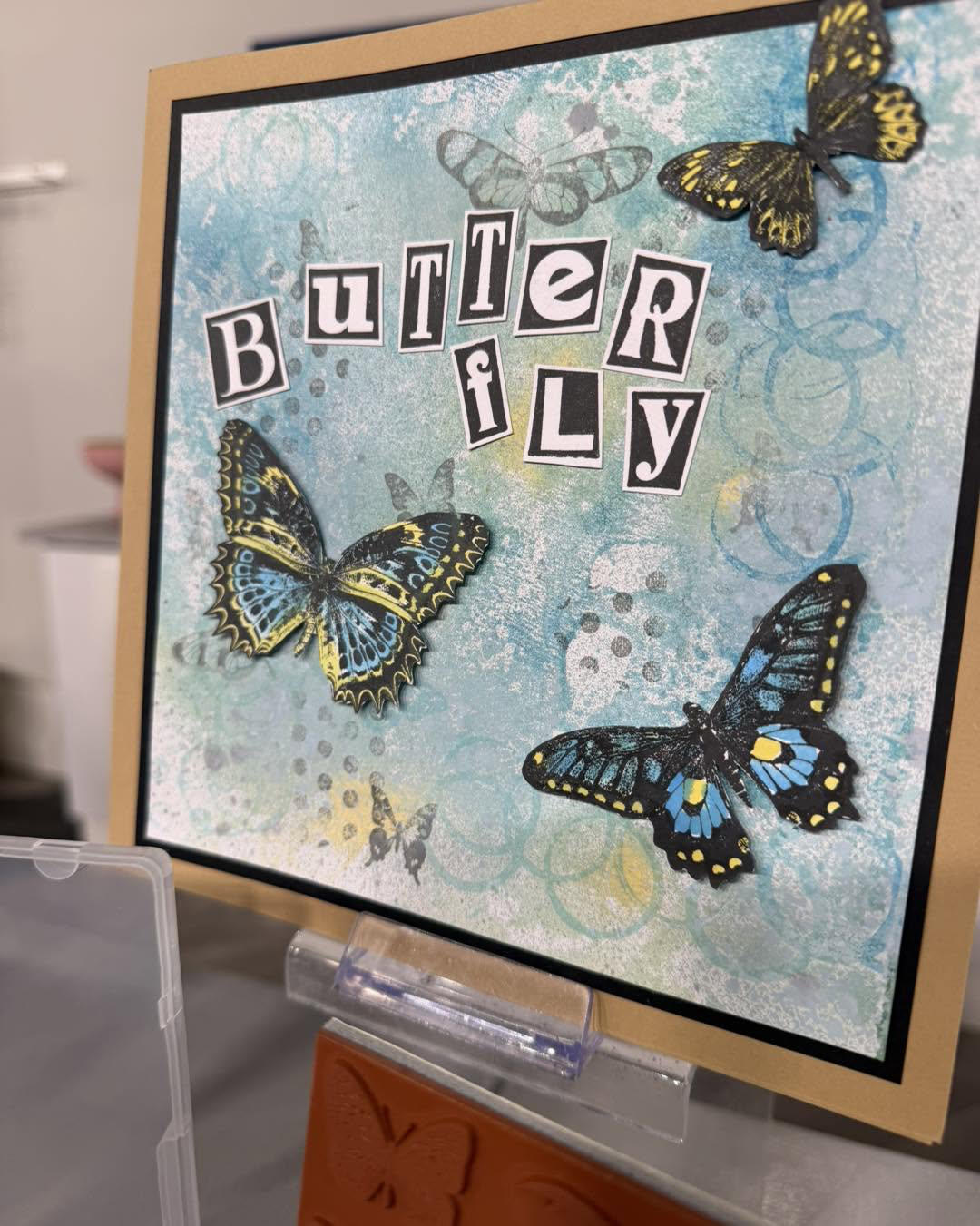 A blue mixed-media card with dimensional butterflies and collaged lettering