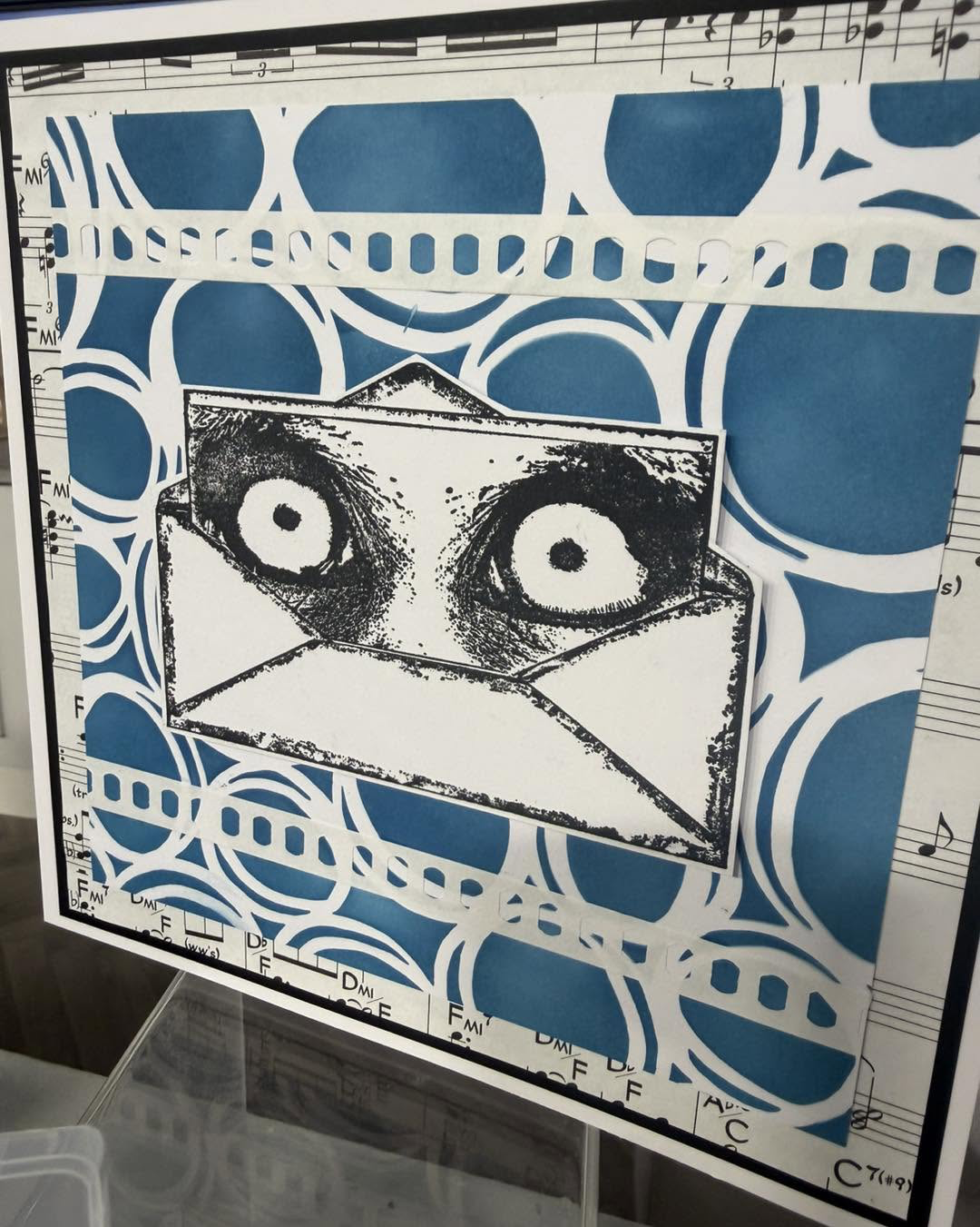 Owl eyes peeking from an envelope on a blue circular-patterned card with musical details