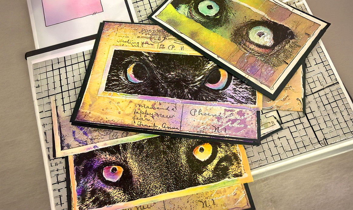 Colourful owl-eye cards layered with script and mixed-media textures on a craft mat